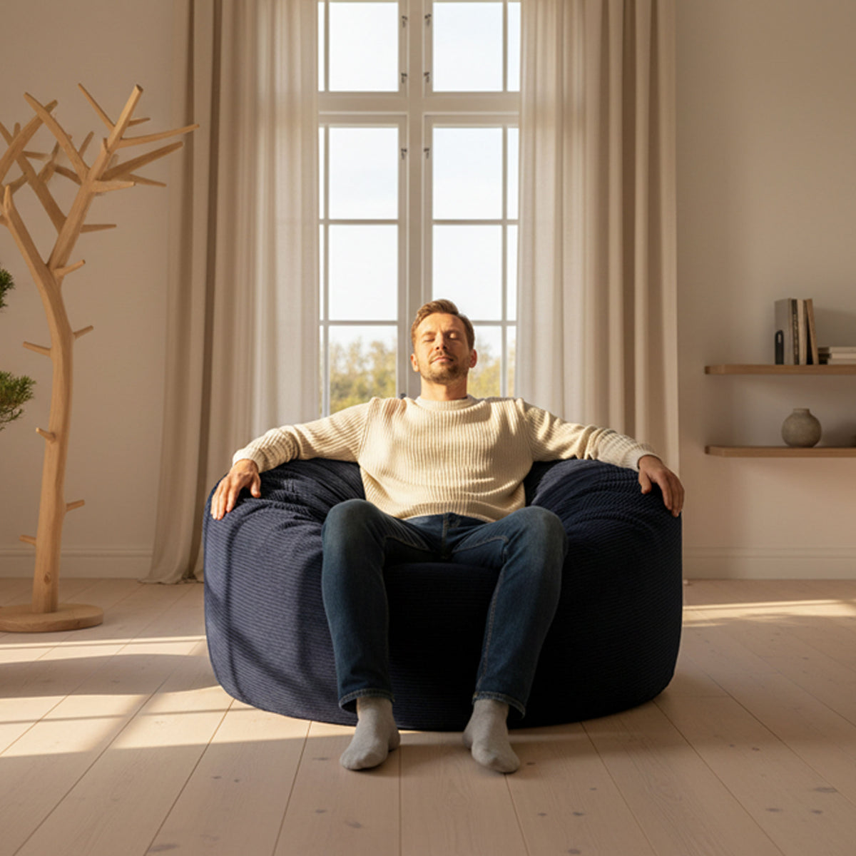 Pouf Géant Rond XXL Velours Côtelé Bleu Marine : homme assis sur un pouf XXL en velours côtelé bleu marine, intérieur lumineux