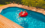 Pouf Rond Piscine Rouge flottant, adulte se relaxant dans l’eau d’une piscine sur terrasse en bois